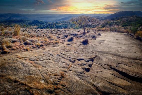 a landscape image incorporating rocky area, with mountains in the background and a setting sun