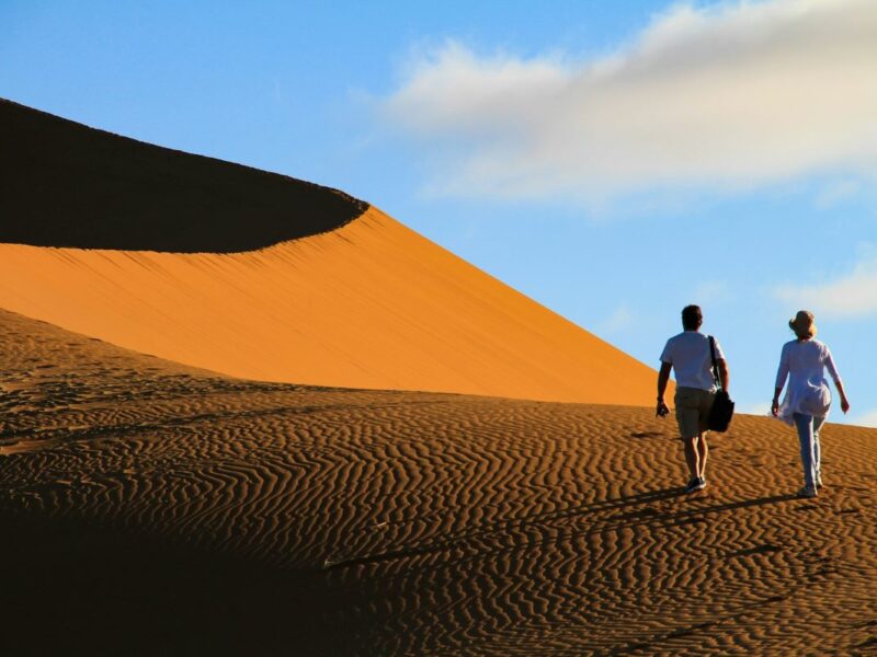 Two people walking up a sand dune at Sossusvlei in Namibia