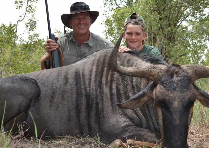 Man and boy posing with a blue wildebeest hunting trophy.